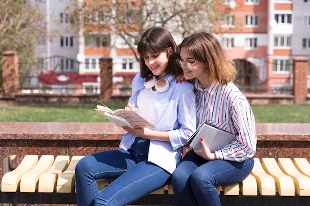 Teenage students sitting on bench with open books