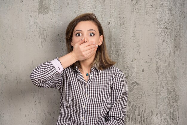 Teenage woman covering mouth with hand on a gray wall