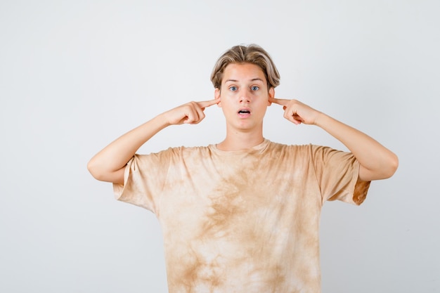 Free photo teenager boy plugging ears with fingers in t-shirt and looking scared , front view.