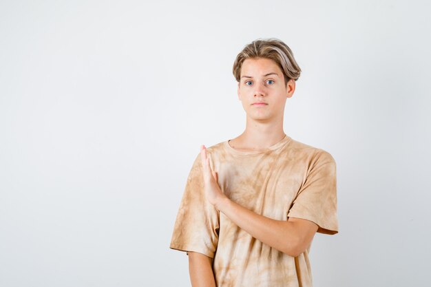 Teenager boy showing stop gesture in t-shirt and looking careful , front view.