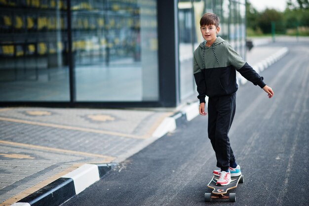 Teenager boy in a sports suit rides on longboard