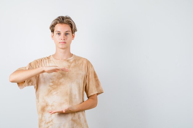 Free photo teenager boy in t-shirt showing large size sign and looking confident , front view.