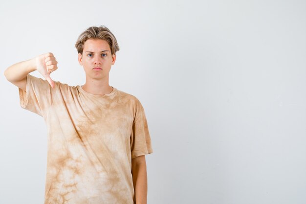 Teenager boy in t-shirt showing thumb down and looking serious , front view.