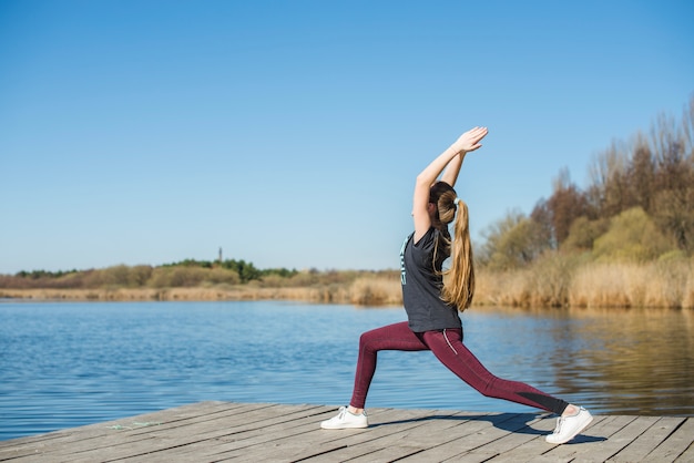 Teenager in crescent lunge pose on pier