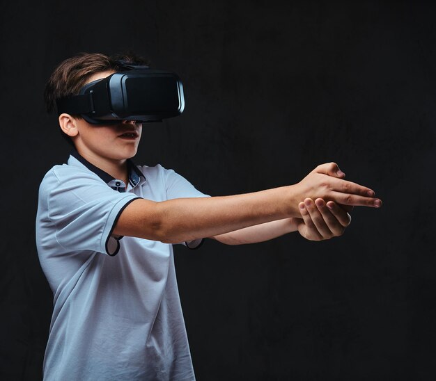 Teenager dressed in a white t-shirt playing with virtual reality glasses. Isolated on a dark background.
