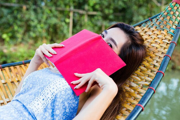 竹のハンモックに横になっている本を読む10代の女性