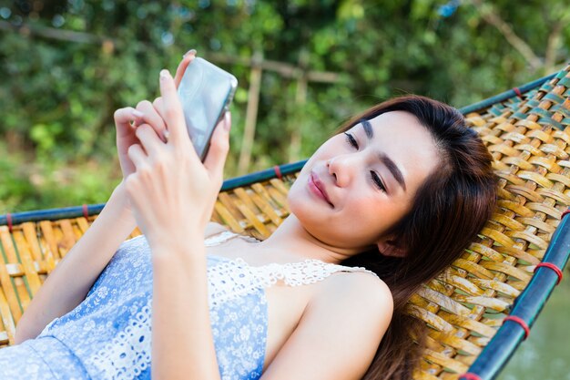 Teenager female lying on bamboo hammock using smartphone