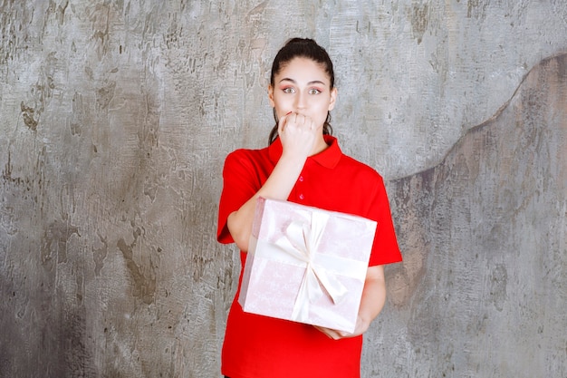 Foto gratuita ragazza adolescente con in mano una confezione regalo rosa avvolta con un nastro bianco e sembra stressata e nervosa.