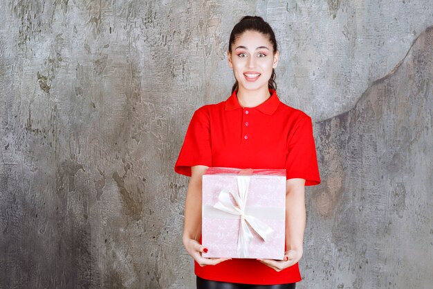 Teenager girl holding a pink gift box wrapped with white ribbon. 