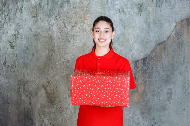 Teenager girl holding a red gift box with white dots on it. 
