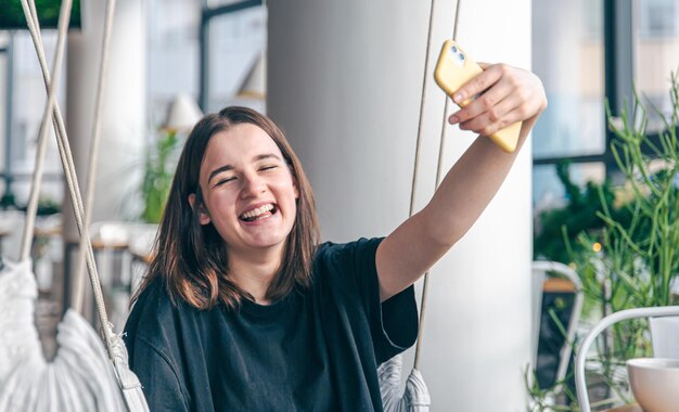 A teenager girl sits in a suspended hammock and takes a selfie on a smartphone