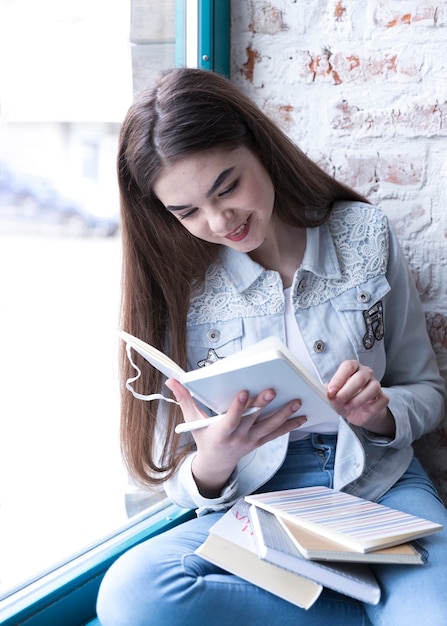 Бесплатное фото Девушка подростка сидя с открытой книгой и усмехаясь пока читающ ее