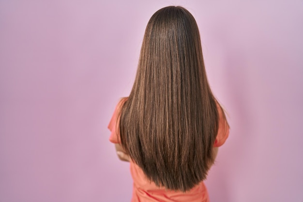Teenager girl standing over pink background standing backwards looking away with crossed arms