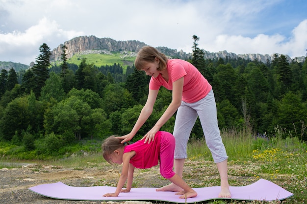10​代​の​少女​は​、​山​を​背景​に​自然​の​中​で​ヨガ​の​練習​を​する​ように​小さな​子供​を​教えています