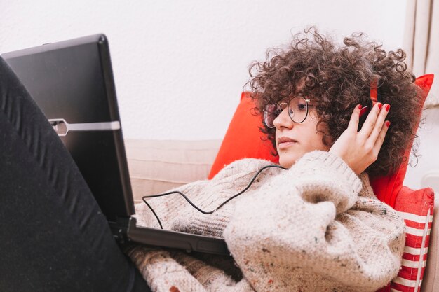 Teenager in glasses listening to music and browsing laptop