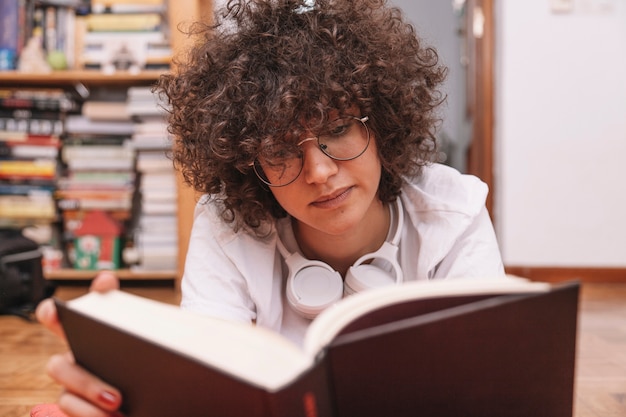 Foto gratuita adolescente in vetri che legge libro sul pavimento