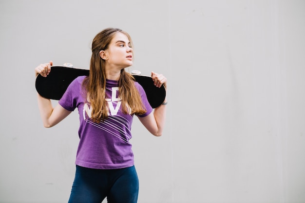 Foto gratuita l'adolescente tiene il suo skateboard guardando a sinistra