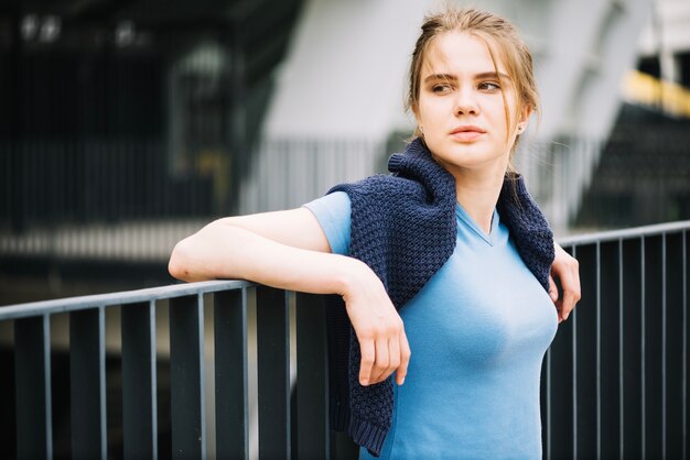 Teenager in jumper leaning on fence