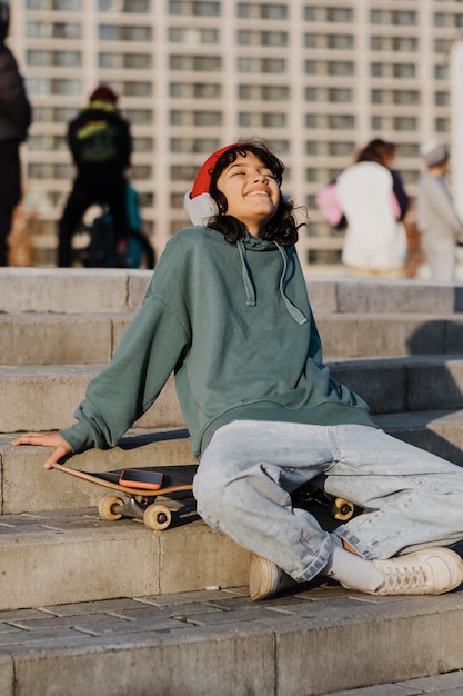 Teenager outdoors enjoying music on headphones while sitting on skateboard