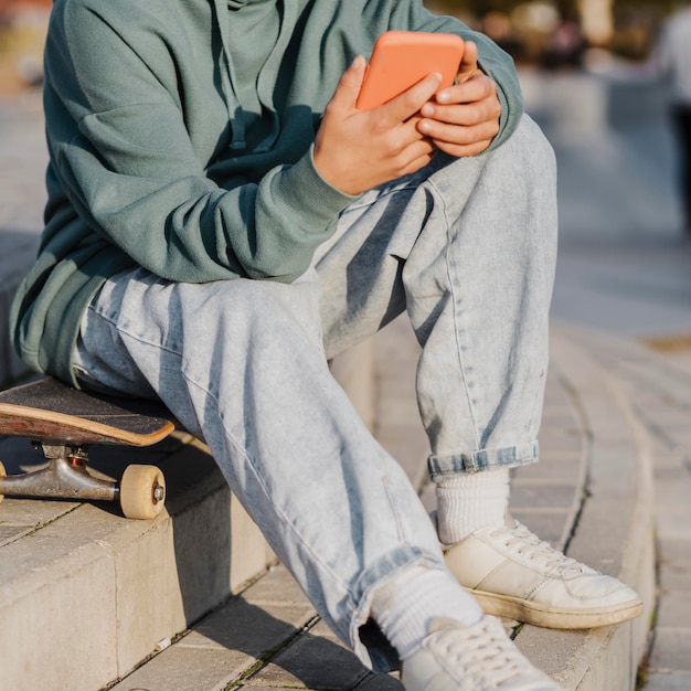 Teenager outdoors holding smartphone while sitting on skateboard