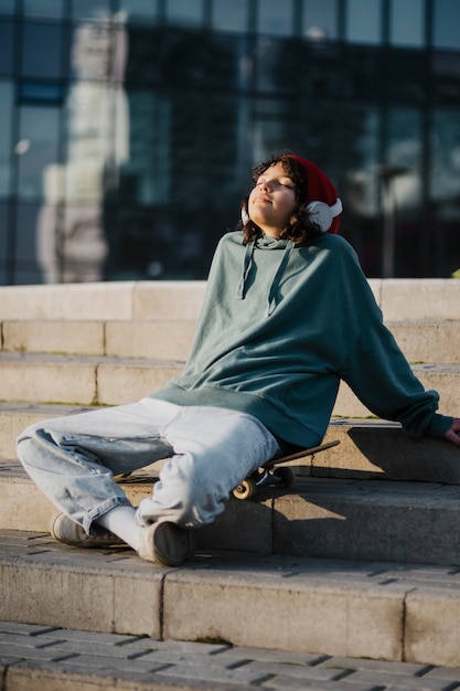 Teenager outside enjoying music on headphones while sitting on skateboard