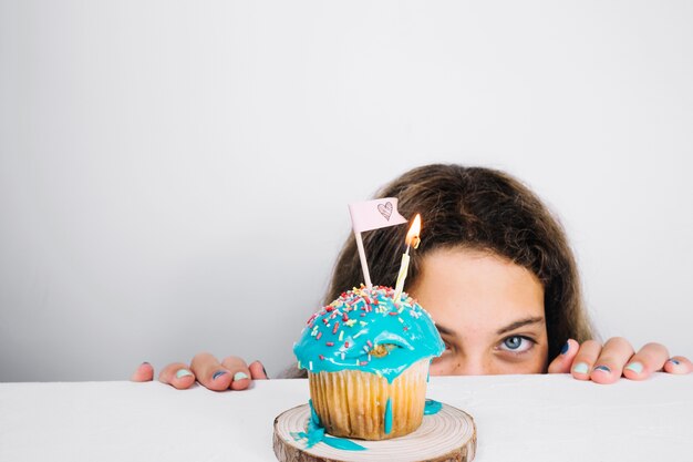 Teenager peeking from behind table with cupcake
