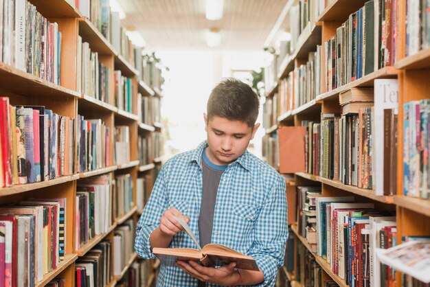 Teenager reading book between bookcases