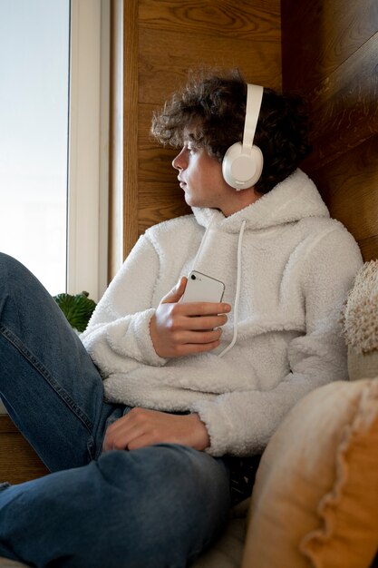 Foto gratuita adolescente seduto nel suo letto e ascoltando musica usando il suo smartphone