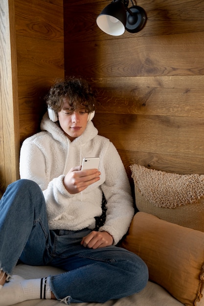 Подросток сидит в своей постели и смотрит на свой смартфон