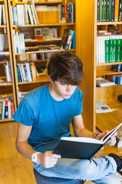 Teenager sitting near bookcases and reading