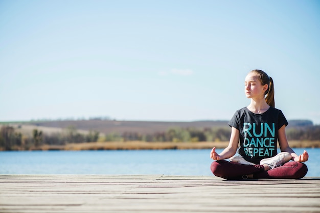 Teenager sitting on pier in lotus position