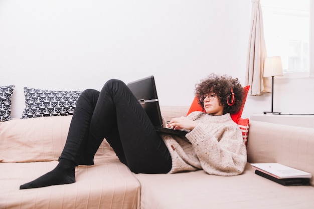 Teenager on sofa listening to music and using laptop