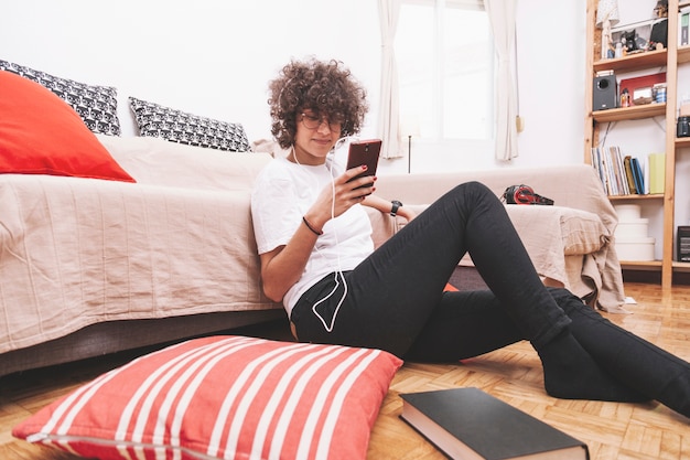 Teenager using smartphone and listening to music on floor