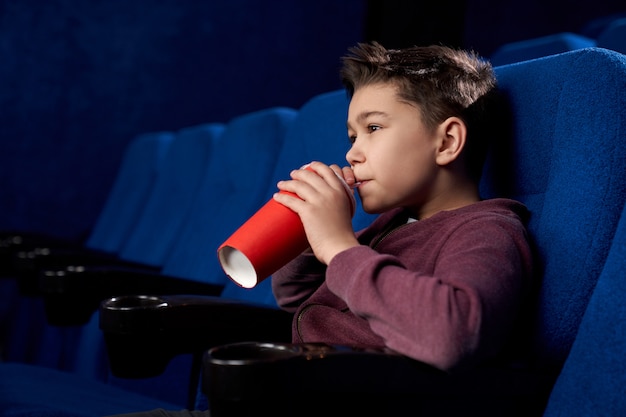 Teenager watching movie, drinking fizzy drink in cinema.