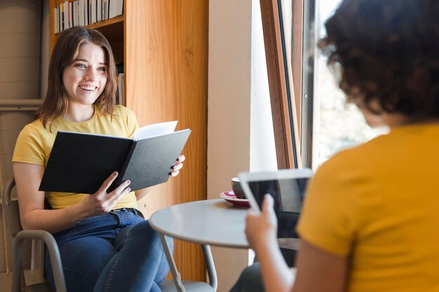 Teenager with book talking with friend in library