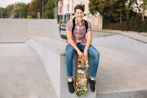 Teenager with skateboard sitting on border