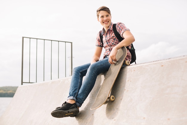 Подросток с скейтбордом, сидящим на рампе