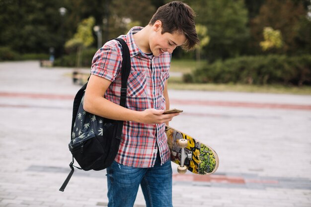 Teenager with skateboard using smartphone