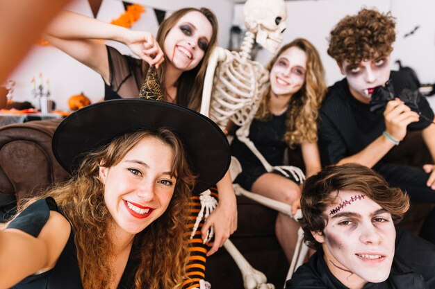 Teenagers in grim and alloween costumes and skeleton doing selfie and smiling