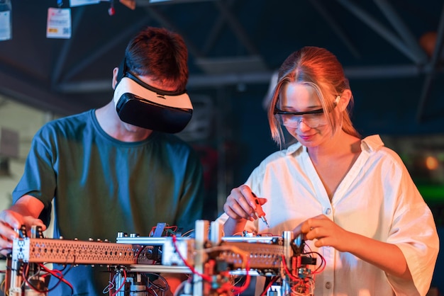 Teens doing experiments in robotics in a laboratory Boy in VR headset and girl in protective glasses