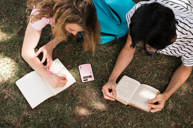 Teens reading with book and notepad on grass 