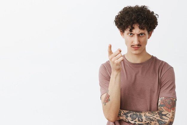 Telling you last time to piss off. Irritated and bothered serious-looking dangerous guy with moustache and curly hair looking from under forehead threatening rival pointign with index finger to warn