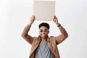 Free photo ten out of ten. young good-looking dark-skinned stylish man with afro hairstyle in casual outfit holding cardboard over head, smiling with teeth. copy space