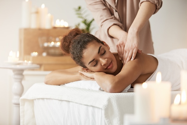 Tender african woman smiling enjoying massage with closed eyes in spa resort.