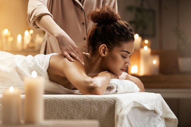 Tender african woman smiling enjoying massage with closed eyes in spa resort.