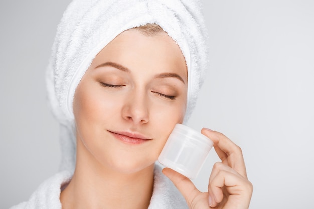 Tender blond woman with bath towel on hair showing cream