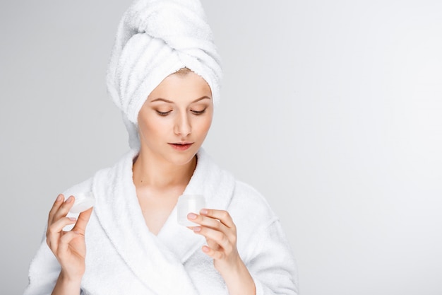 Tender blond woman with bath towel on hair showing cream