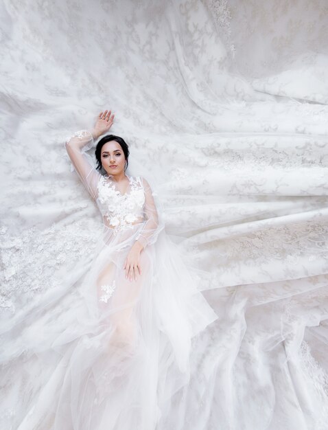 Tender brunette caucasian bride is laying on the fabric of a luxury wedding dress