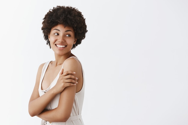 tender and charming beautiful african american woman with curly hairstyle turning right with sensual and happy smile, touching arm gently standing