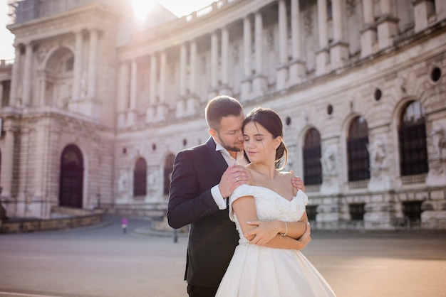 Tender couple in love is  hugging with closed eyes in front of historical architectural building